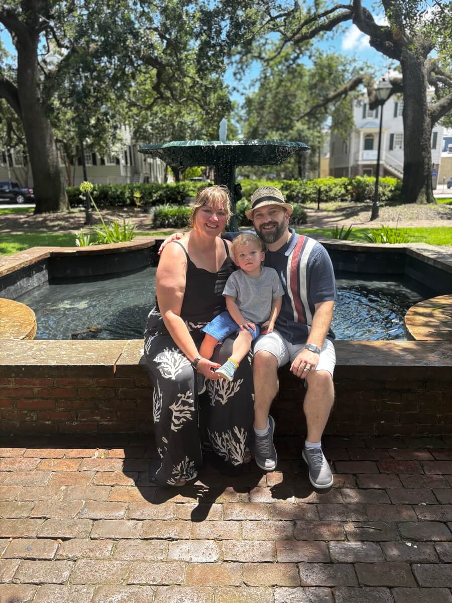 Taylor Desens sits on a fountain in Savannah Georgia with her husband and son.